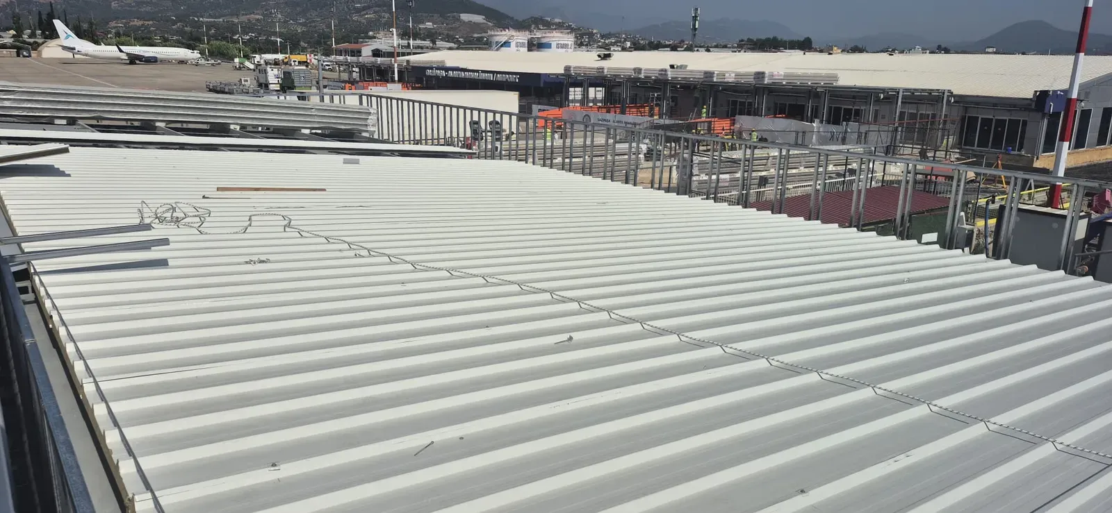 Gazipaşa-Alanya Havalimanı'nda beyaz hadveli taşyünü çatı panelleri; arkada terminal binası ve apron